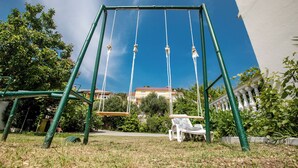A swing set in a grassy area with a white building in the background. - Sunset View Rab Apartment (Rab)