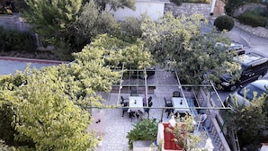 An outdoor seating area with tables and chairs, surrounded by trees and a stone wall. - Sunset View Rab Apartment (Rab)