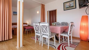 A room with a dining table set for two, two chairs, a bed with a wooden headboard, a nightstand, a lamp, and a framed picture on the wall. - Sunset View Rab Apartment (Rab)