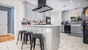 A modern kitchen with grey cabinets, a black island with bar stools, a microwave, and a dishwasher.