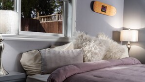 A bedroom with a bed, a nightstand, a lamp, a window, and a wall-mounted picture.