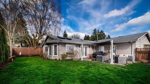 A two-story house with a covered patio, a lawn, and a wooden fence.