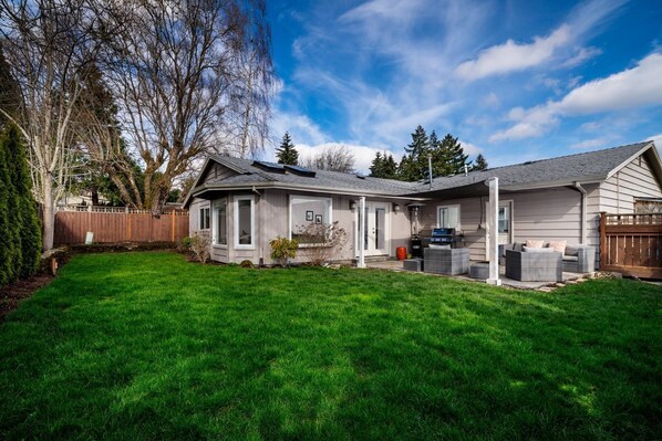 A two-story house with a covered patio, a lawn, and a wooden fence. - Amazing Single Level Suburban Home, Pet Friendly, Fenced Backyard, Close 2 Nike, Shopping, Portland (Beaverton)