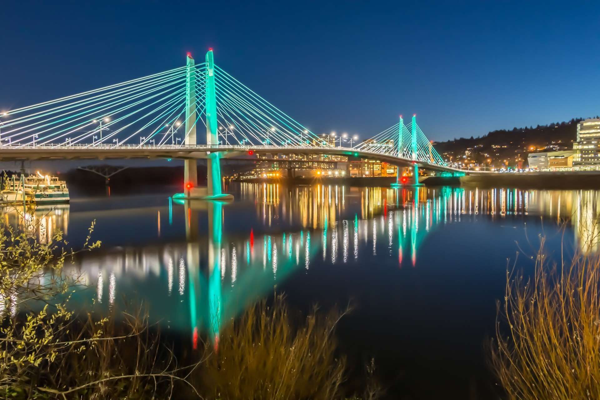 A bridge with a modern design, featuring multiple cables and illuminated by green lights.