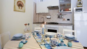 A kitchen with white cabinets, a stove, and a refrigerator. There is a dining table set with plates, cups, and a candle.