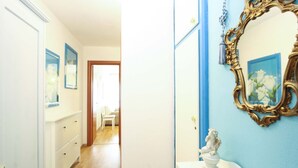 A hallway with a wooden floor leading to a room with a white dresser and a blue wall with a gold-framed mirror.