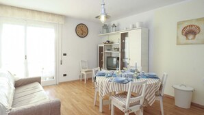 A dining area with a table set for four, a television, and a clock on the wall.