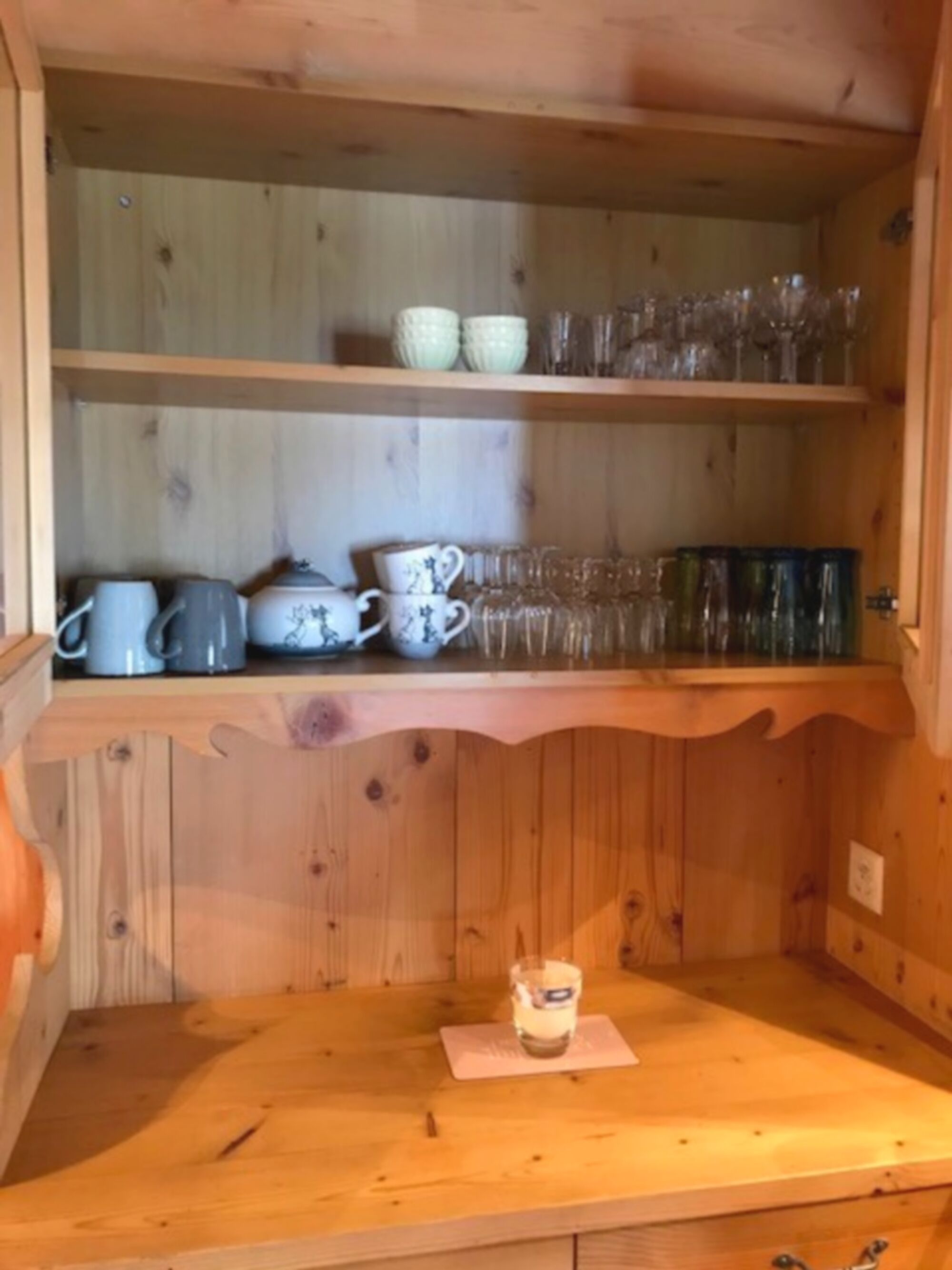 Et træskab med hylder, der indeholder forskelligt glas og keramik.