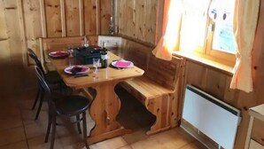 Puisesta materiaalista valmistettu ruokailutila, jossa on neljälle katettu ruokapöytä, penkki ja ikkuna, jossa on verhot.