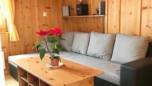 Puupaneloitu huone, jossa on sohva, puinen pöytä, jonka päällä on ruukkukasvi, sekä hylly, jossa on elektronisia laitteita.