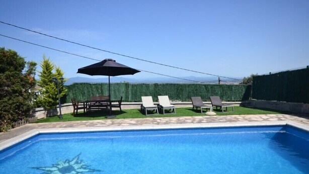 Una piscina con sillones de descanso y una mesa, rodeada por un seto y una valla de madera.