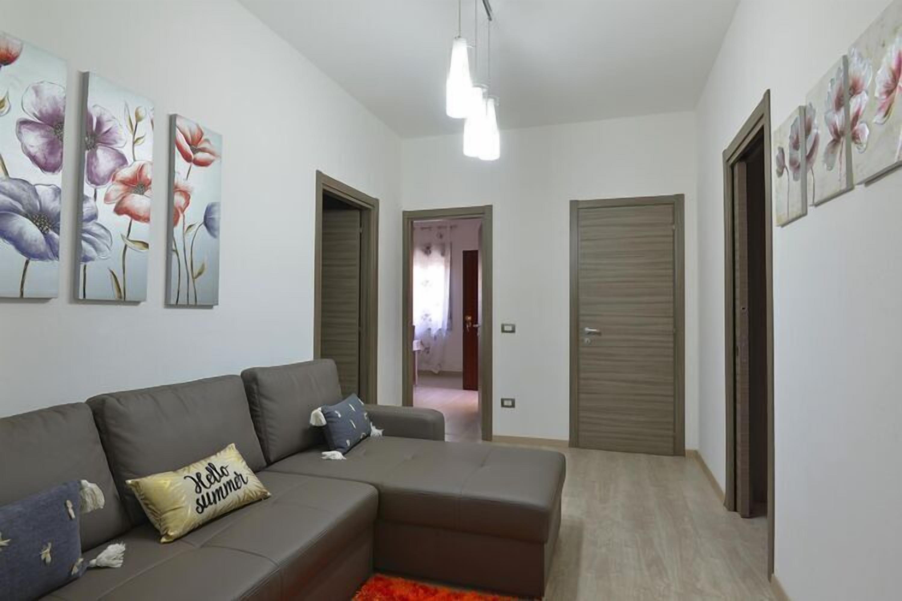A modern living room with a grey sectional sofa, a red rug, and floral wall art.