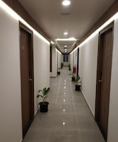 A hotel corridor with doors on both sides, a lift sign overhead, and potted plants along the floor.