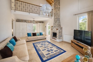 A living room with a stone fireplace, a sofa with cushions, a television, and a decorative rug.