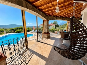 A covered outdoor area with a pool, stone pillars, and a hanging chair.