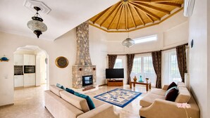 A living room with a stone fireplace, a television, a sofa, and a dining area with a kitchen. - Stunning Villa Semira, Perfect Condition, Private Pool & 1000m2 Garden,WIFI (Muğla)
