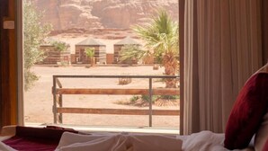 A room with a view of a desert landscape, including rock formations and a fenced area with palm trees.