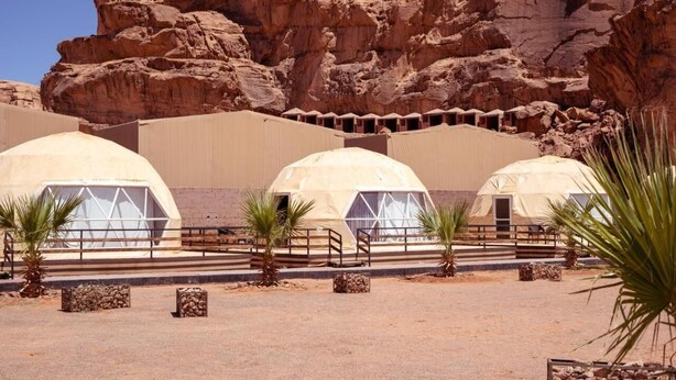 Three dome-shaped tents with a central walkway, set against a rocky backdrop.