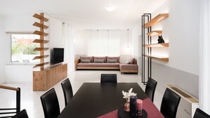 Moderni olohuone, jossa on sohva, ruokapöytä tuoleineen ja seinälle kiinnitetty televisio, joka on asennettu puiseen rakenteeseen.