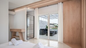 Moderni hotellihuone, jossa on suuri sänky, puinen työpöytä ja liukuovi, joka johtaa ulkotilaan, jossa on oleskelualue.