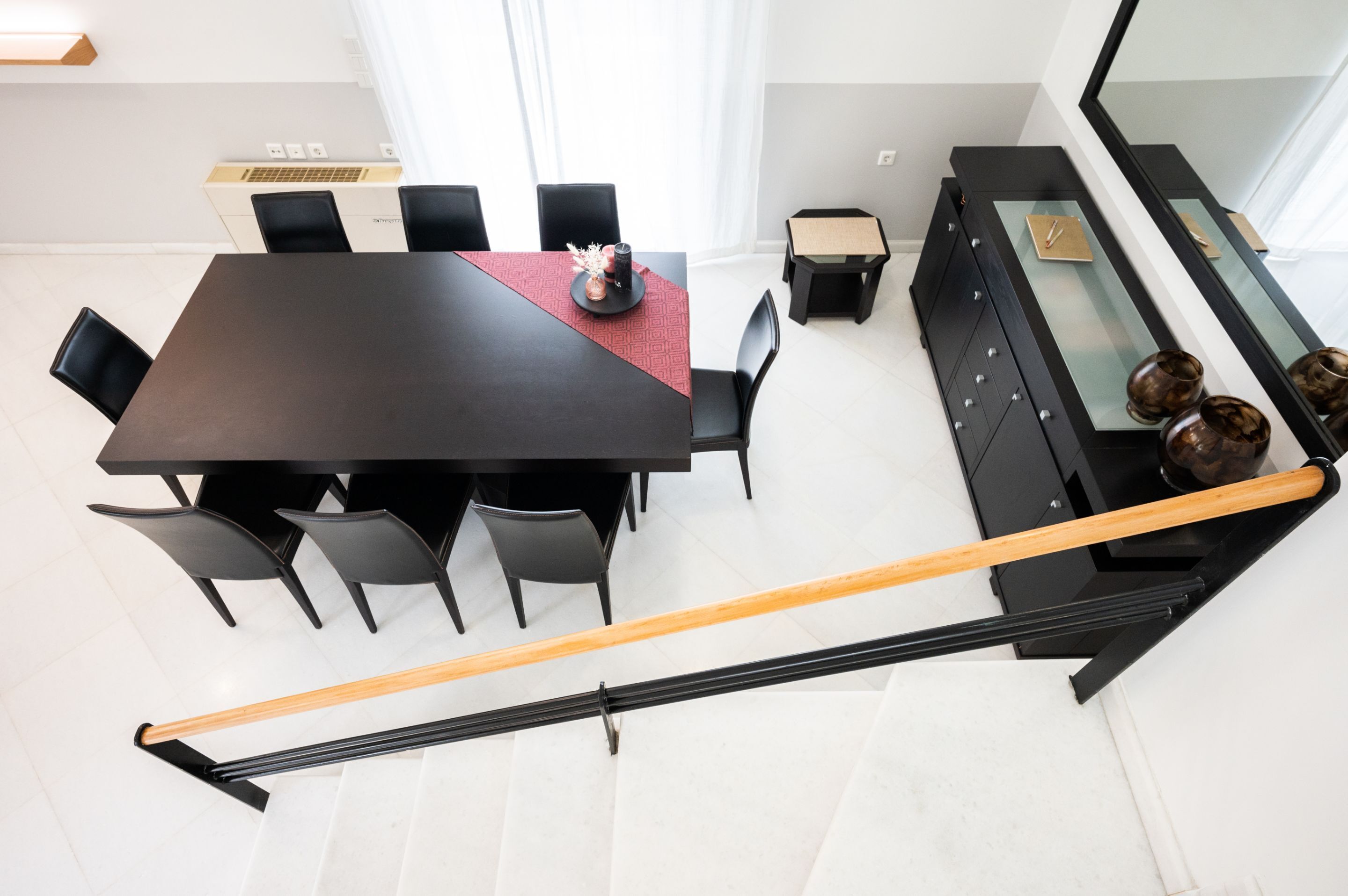 Un espace repas moderne avec une table et des chaises noires, une petite table d’appoint agrémentée d’objets décoratifs et une console en verre surmontée de vases.