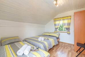 A room with two beds, a window with curtains, a wooden door, and a small table.
