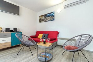A modern living room with a red sofa, two chairs, a small table with a magazine, and a cityscape painting on the wall.