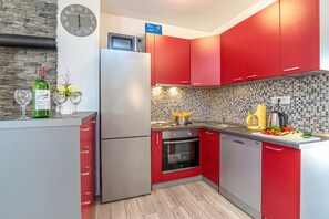 A modern kitchen with red cabinets, a stainless steel refrigerator, a microwave, and a tiled backsplash.