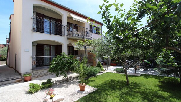 A two-story building with a balcony, a small garden with potted plants, and a tree. - Apartments Denise (Rovinj)