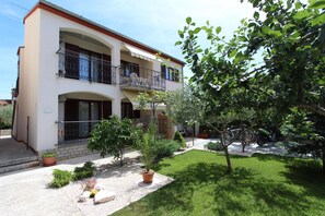 A two-story building with a balcony, a small garden with potted plants, and a tree. - Apartments Denise (Rovinj)