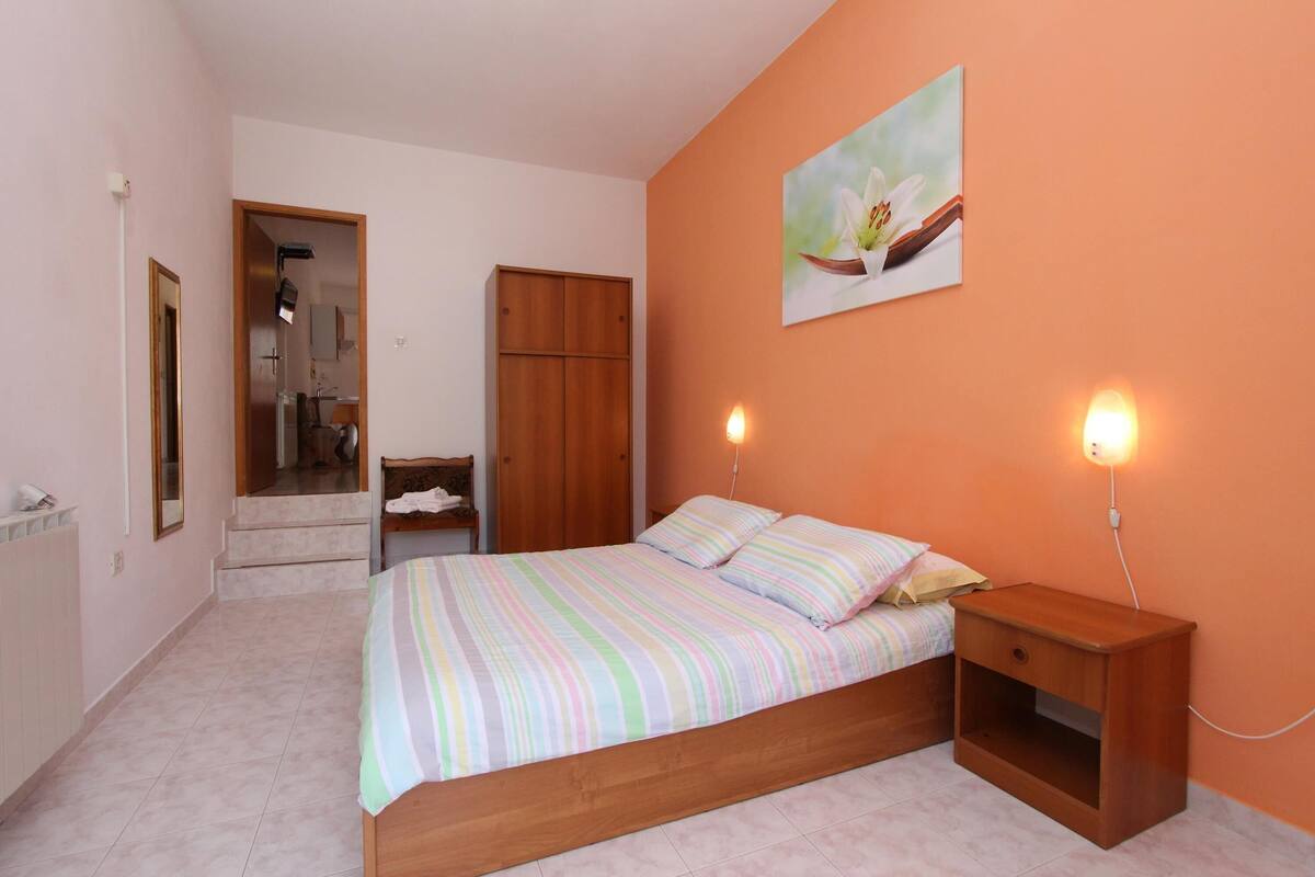 A bedroom with a bed, nightstands, a wooden wardrobe, a mirror, and a painting on the wall.