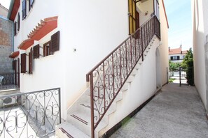 A narrow stairway with wrought iron railings leading to a white building with red accents and brown shutters. - Apartments Denise (Rovinj)