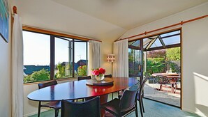 Uma sala de jantar com uma mesa grande e cadeiras, um vaso de flores e janelas amplas com vista para o exterior.