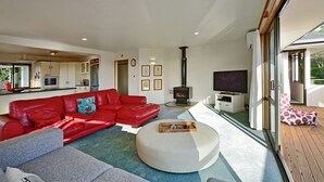 Uma sala de estar moderna com um sofá de couro vermelho, uma mesa de centro branca e uma TV sobre um suporte de madeira.