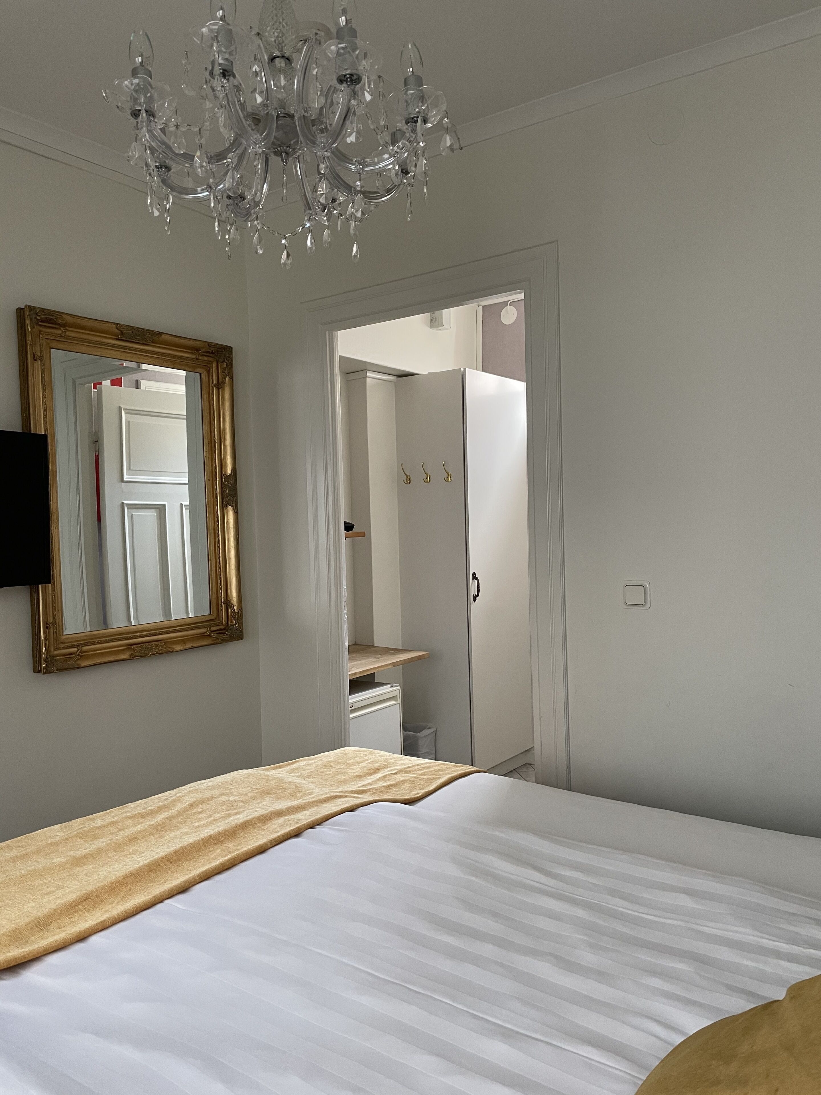 A bedroom with a bed, a chandelier, a mirror, and a wardrobe.