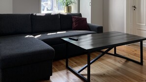 Un salon moderne avec un canapé d’angle, une table basse, une suspension et une plante en pot près d’une fenêtre.