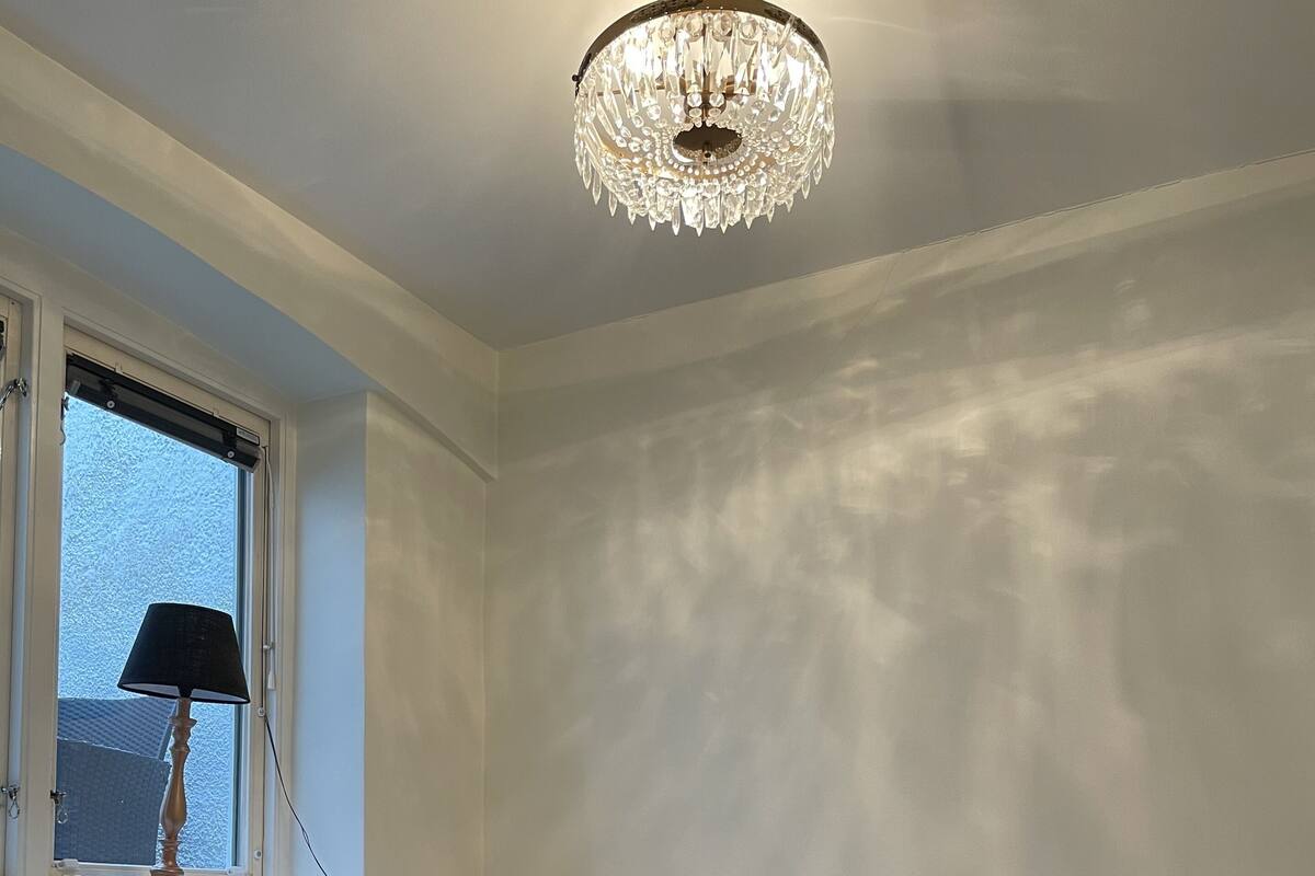 A bedroom with a bed, a window with a lamp, and a chandelier.