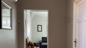 Un couloir avec un plancher en bois, une porte sur la droite, et une chaise et un canapé au fond.