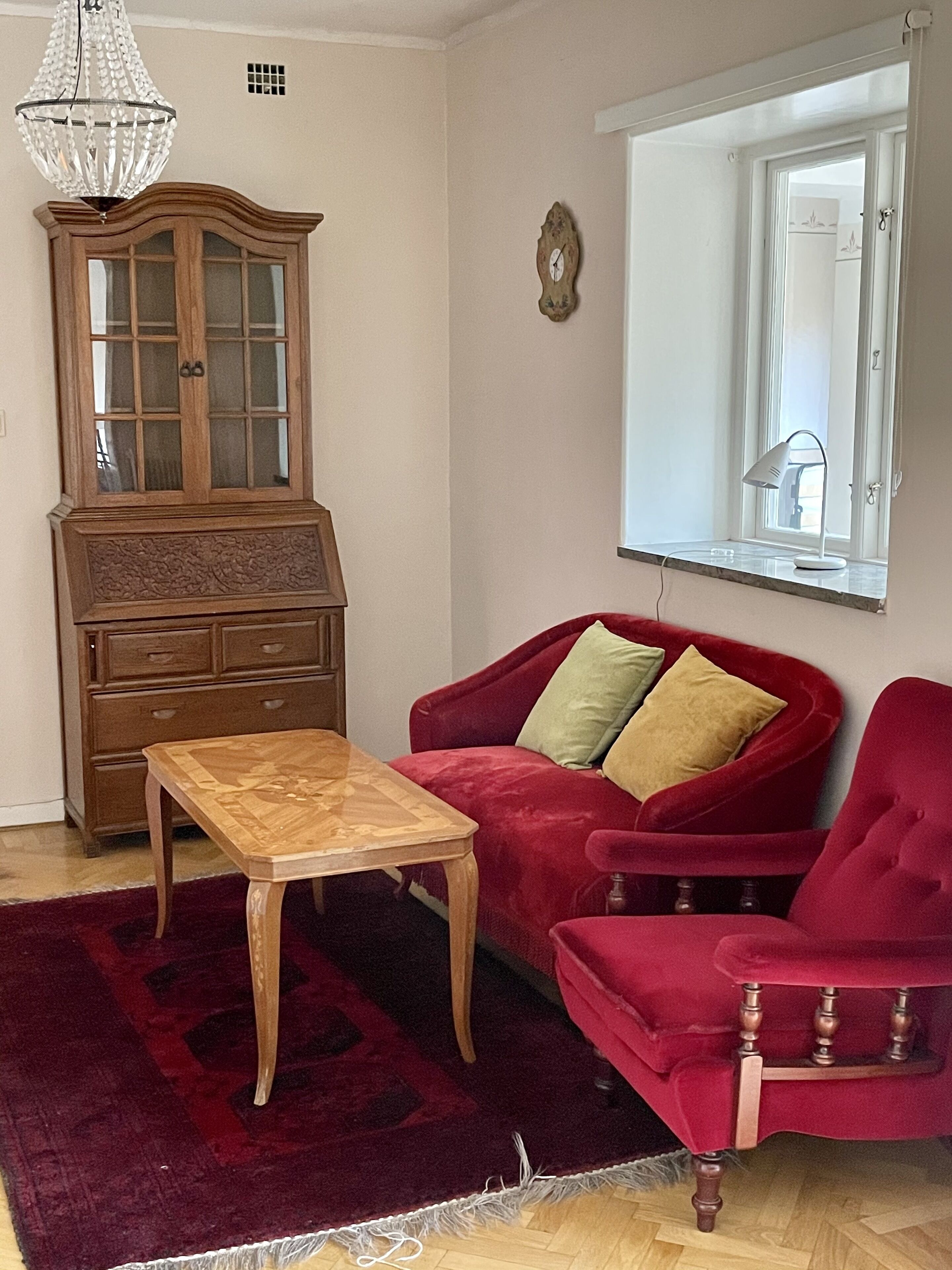 Ein Wohnzimmer mit einem Holzkabinett, einem roten Sofa, einem Holztisch und einem roten Sessel.