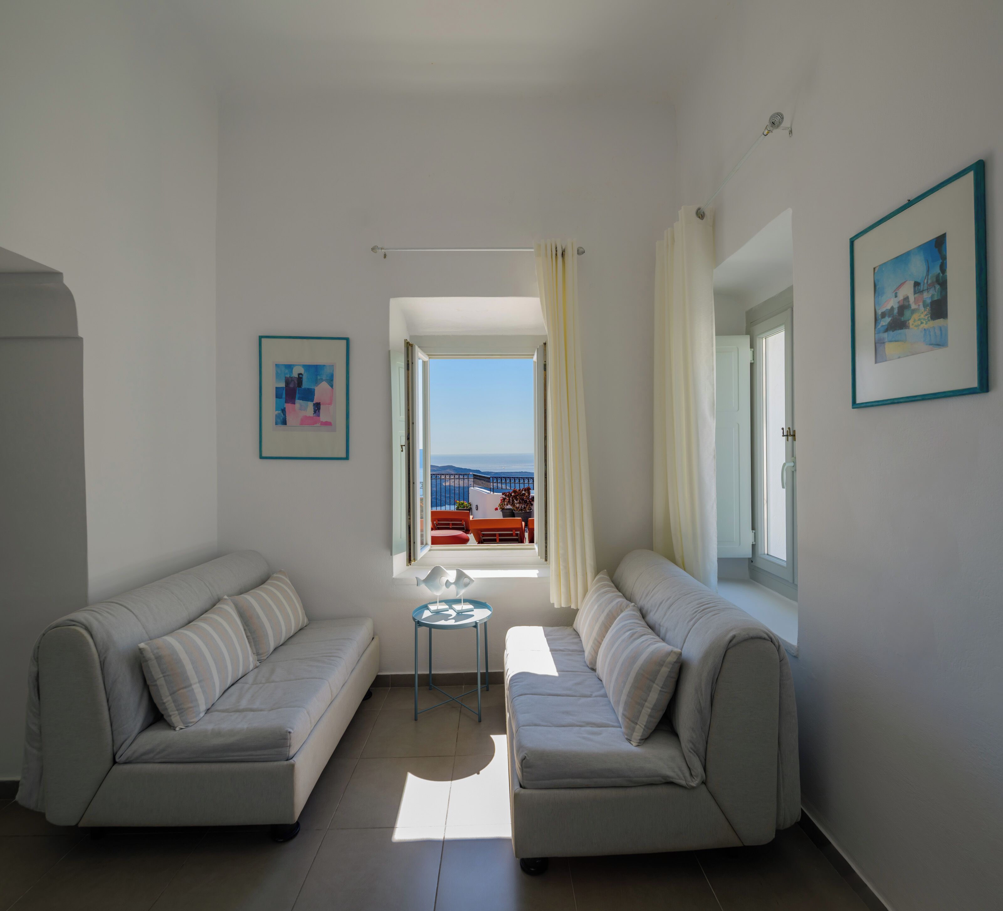 A modern living room with two sofas, a small round table, and a view of the sea through a window.