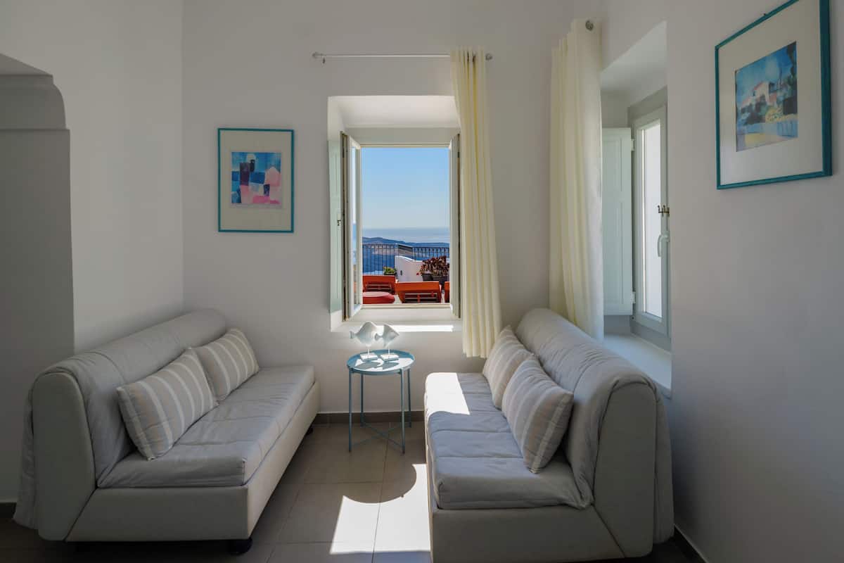 A modern living room with two sofas, a small round table, and a view of the sea through a window.