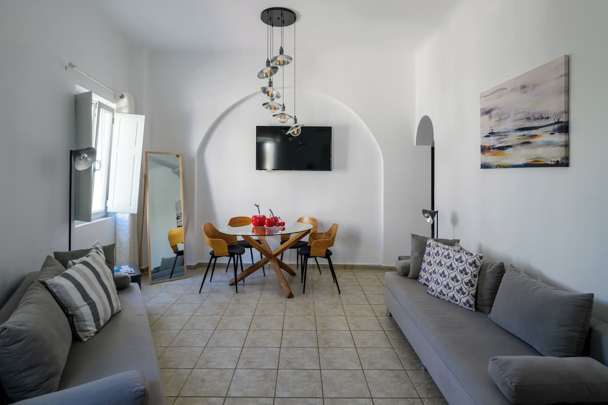 A modern living room with a dining area, a sofa, a TV mounted on the wall, and a painting.