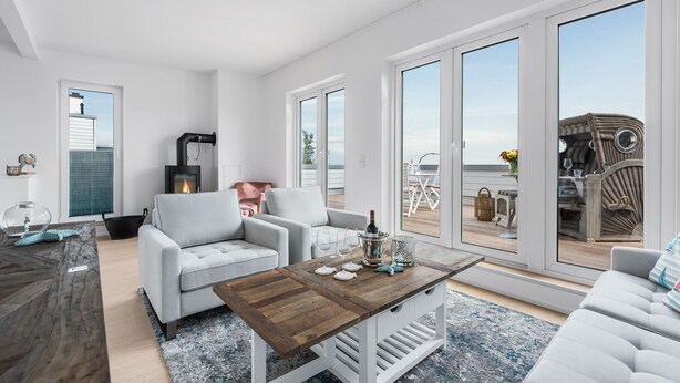 Ein modernes Wohnzimmer mit Kamin, weißen Sofas, einem Holztisch und großen Schiebeglastüren, die auf eine Terrassenanlage führen.