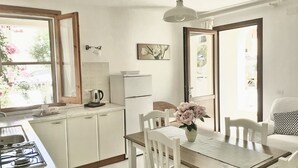 Une cuisine lumineuse avec des meubles blancs, une cuisinière à gaz, une bouilloire et une table à manger avec des chaises.