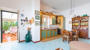 A spacious living area with a kitchen, dining table, and a large window overlooking a garden. - Terrazza Morgera by Napoliapartments (Casamicciola Terme)