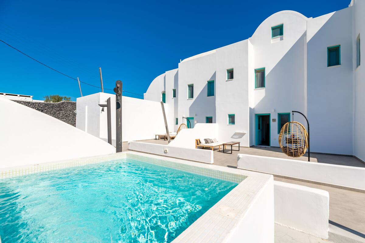 Un espace piscine avec une eau d’un bleu limpide, des bâtiments blancs agrémentés de touches de bleu et des espaces de détente en plein air.