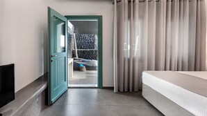 Une chambre d’hôtel moderne équipée d’un lit, d’une télévision, d’une porte verte donnant sur un balcon et offrant une vue sur un mur en pierre.