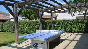 A table tennis table under a wooden pergola in an outdoor setting.