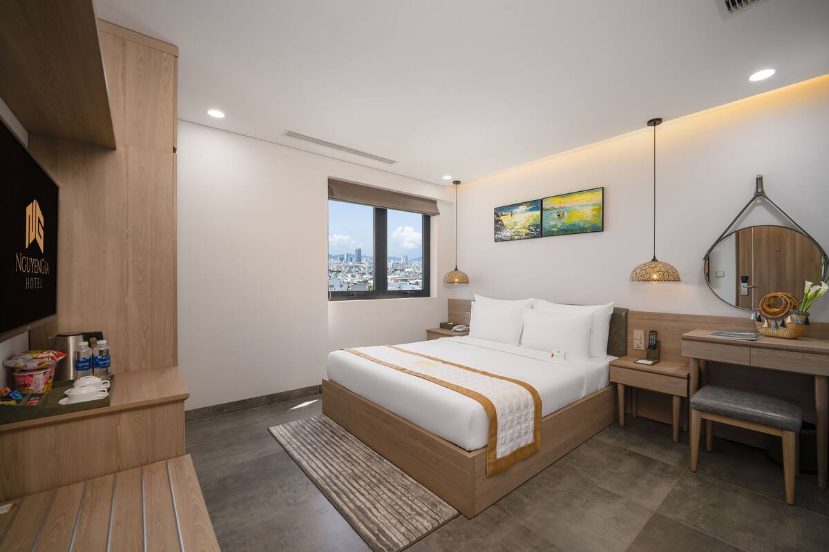 A modern hotel room with a large bed, a desk, a chair, a TV, and a window with a city view.