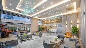 En moderne hotellobby med siddeområder, en reception og et stort vindue med udsigt over byen.